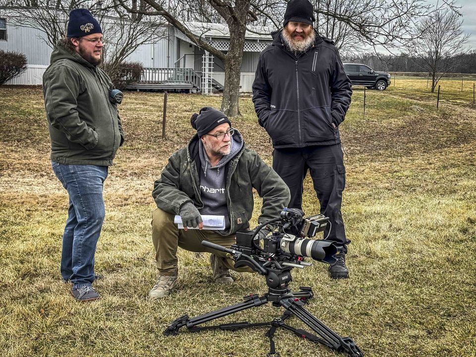 Crew members gather around a tripod-mounted camera outdoors.