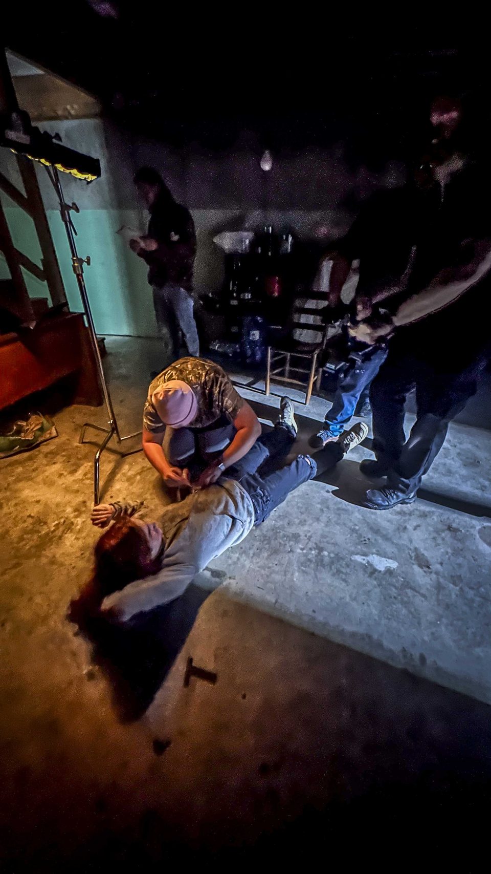 A crew member adjusts an actor's costume on the basement set floor.