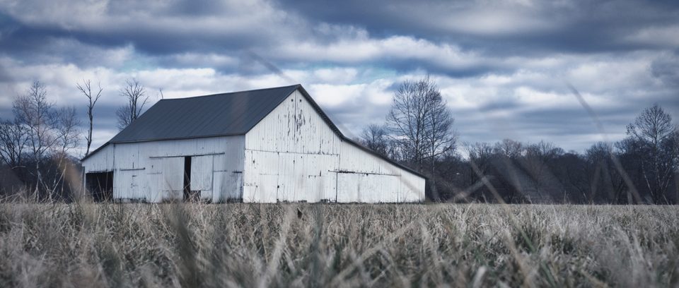 A white barn stands alone in a wide, empty field.