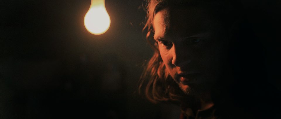 Jude, played by Zach Hurley, lit by a single hanging bulb in the basement.