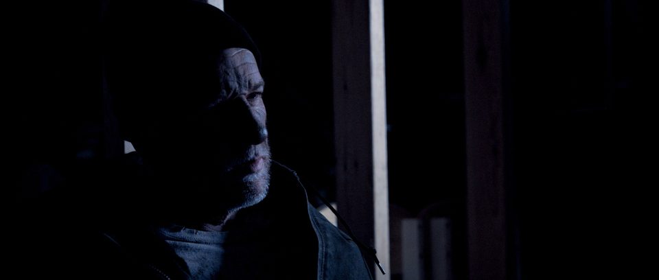 Mac, played by Daniel J. Lennox, in profile under dim light.