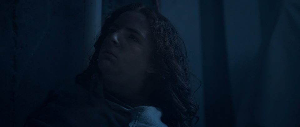 Samuel, played by Deacon Grasty, lying in the dark basement, bathed in blue light.